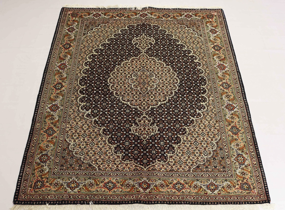 Exquisite Tabriz rug showcasing a detailed central medallion surrounded by intricate floral patterns and delicate borders. The rug is handwoven in Tabriz, Iran and features a rich color palette of reds, blues, and golds. This image accompanies an article discussing the unique characteristics of Tabriz rugs, which are renowned for their high quality, intricate designs, and ability to add sophistication to any space. Tabriz rugs can complement a wide range of décor styles, from traditional to modern.