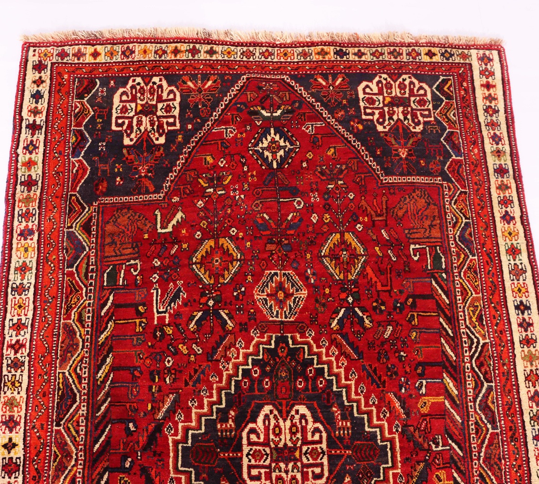 Colorful tribal rug with a bold, geometric pattern and a variety of vibrant hues. The rug is spread out on a hardwood floor, with natural light streaming in from a nearby window. This image accompanies an article discussing the unique characteristics of tribal rugs, which are made by nomadic tribes and often feature highly durable wool construction and eye-catching designs. Tribal rugs are particularly well-suited for high-traffic areas like hallways and entryways.